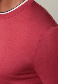 Rotes Baumwoll-T-Shirt mit enganliegendem Schnitt, ausgestattet mit einem Rundhalsausschnitt und kontrastierenden Streifen in Weiß und Marineblau am Kragen.