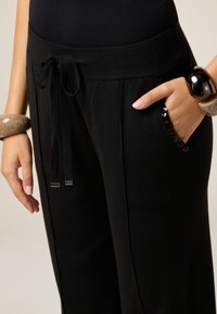 Zwarte wijde broek met een zachte textuur, een tailleband met trekkoord en zijzakken met paillettenaccenten. Kenmerken zijn onder andere metalen hardware.