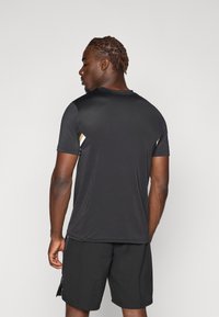 T-shirt de sport noir à manches courtes, avec des sections en maille texturée et des accents de rayures dorées, associé à un short noir.