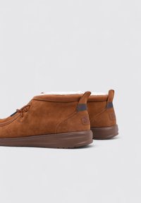 Bruine suède enkelboots met een zachte binnenvoering, ronde neus, contrasterende diepblauwe accenten en een brown rubberen zool.