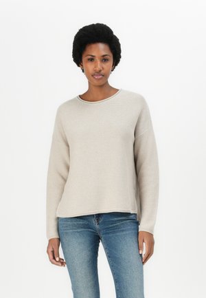 Light beige knitted sweater with a crew neckline, relaxed fit, and ribbed trim. Worn over blue jeans, displaying a subtle texture.