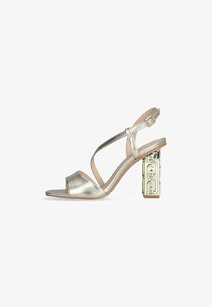 Metalik srebrne sandale na visokom petu z odprtim nosom in trakcem okoli gležnja. Imajo geometrijsko oblikovan blokasti peto za dodatno podrobnost.