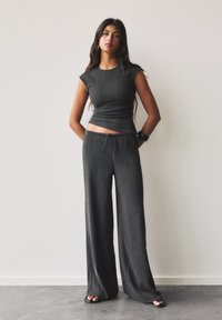Crop top en maille côtelée grise avec des manches courtes associé à un pantalon large gris doté d'une taille à cordon. Texture lisse, détail minimal.
