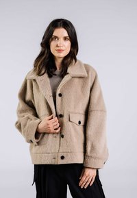 Beige ullblandad jacka med en strukturerad yta. Har krage, knappstängning och framfickor. Avslappnad passform med vida ärmar.