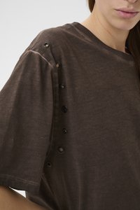 Hnedé bavlnené tričko s voľným strihom, zdobené veľkými okami pozdĺž ramena. Mäkká textúra a krátke rukávy.