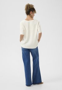 Witte top met korte mouwen en een ronde hals, gecombineerd met blauwe wijde jeans. Eenvoudig, textuurontwerp met een losse pasvorm.