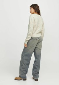 Maglione grigio chiaro lavorato a maglia con motivi a rombi, abbinato a jeans in denim blu a vestibilità ampia e stivali alla caviglia marroni. Outfit casual mostrato da dietro.