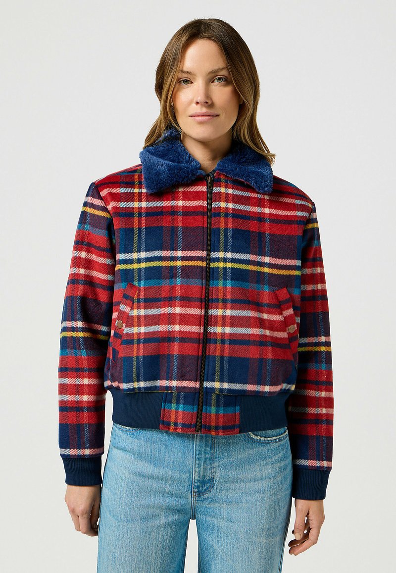 Giacca a scacchi rossa e blu con colletto in pelliccia blu navy, chiusura con zip e tasche laterali. Tessuto morbido con polsini e orlo a coste.