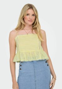 Yellow and white striped peplum top with lace trim and eyelet details; worn over a denim skirt with button accents. Straps and lightweight fabric.