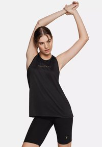 Canotta atletica nera senza maniche con scollatura tonda, caratterizzata da un logo dorato. Indossata con pantaloni bici neri abbinati. Tessuto liscio.