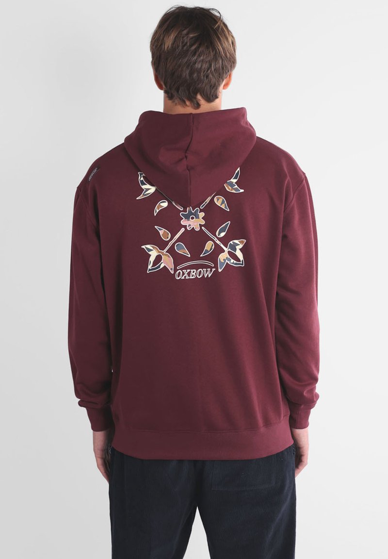 Sweat à capuche bordeaux avec une capuche, présentant un design graphique floral et de feuilles au dos. Fabriqué en tissu doux, adapté pour un usage décontracté.