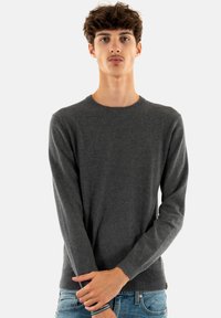 Pull en maille grise avec des manches longues et un col rond. Texture douce et design ajusté. Associé à un jean bleu.