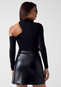 Zwarte bodysuit met lange mouwen en een open schouderdesign, gecombineerd met een zwarte mini-rok van nepleer met hoge taille. Soepele textuur en een nauwsluitend silhouet.