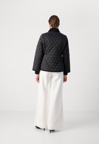 Zwarte gewatteerde jas met een contrasterende kraag, oversized mouwen en een tailleband, gecombineerd met witte wijde broek en zwarte hakken.