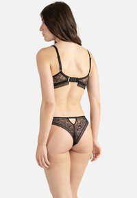 Ensemble de lingerie en dentelle noire comprenant un soutien-gorge avec des bretelles réglables et un fermoir, et un string assorti avec des détails en dentelle et une découpe en forme de clé.