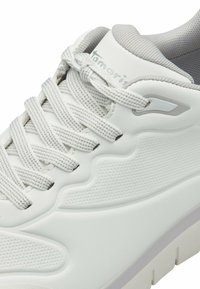 Fehér sneaker texturált felsőrésszel, lapos fűzőkkel és párnázott nyakkal. A talpa vastag és enyhén megemelt a kényelem érdekében.