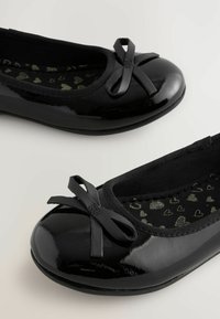 Balerini din patat negru, cu vârful rotund, având un accent din fundiță neagră și o interior texturată cu un model de inimă. Margine elastică neagră.