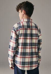 Herre skjorte i flannel med tern i creme, der har blå og røde mønstre. Lange ærmer og knapmanchetter. Blødt, tekstureret stof.