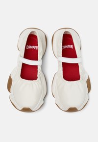 Weiße Schuhe mit strukturiertem Obermaterial, elastischem Riemen über dem Spann und braunen Gummisohlen. Die roten Innensohlen tragen die Marke "CAMPER".