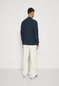 Suéter de punto azul marino con textura acanalada, combinado con pantalones cargo en color blanco roto. El conjunto presenta mangas largas y un corte relajado.