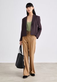 Lilla cropped blazer over en grønn cami, kombinert med beige vide bukser. Svart tote bag og svarte sko fullfører looken.