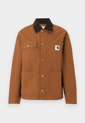 Veste Carhartt marron avec col en velours côtelé noir, quatre poches avant dont une avec un patch logo, et des boutons-pression métalliques sur le devant.