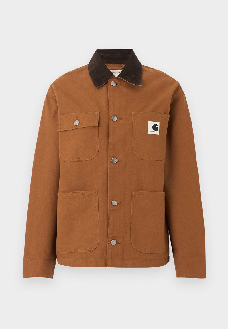 Giacca Carhartt marrone con colletto in velluto a coste nero, quattro tasche frontali di cui una con patch logo e bottoni a pressione in metallo sul davanti.