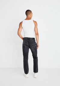 Zwarte denim jeans met een rechte pijp, vijf zakken en contrasterende stiksels, gecombineerd met een witte tanktop en witte sneakers.