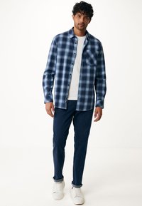 Blå rutiga knapp-up skjorta med ficka, bärs över en vit T-shirt. Matchas med mörkblå byxor och vita sneakers. Slät tygstruktur.