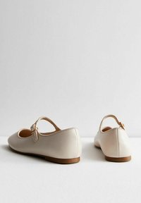 Bailarinas de cuero beige con punta redonda, una sola correa en el tobillo que presenta una hebilla dorada, y una suela plana marrón. Textura suave.