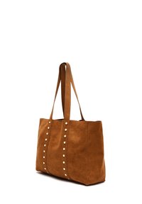 Braune Wildleder-Tasche mit zwei langen Griffen, die an der Vorderseite vertikale Reihen runder, weißer Nieten als Akzent aufweist. Einfaches, rechteckiges Design.