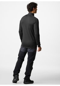 Pullover nero a maniche lunghe con colletto alto, abbinato a pantaloni cargo grigio scuro e neri, e stivali da trekking neri. Abbigliamento casual per attività all'aperto.