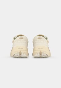 Tenisi bej cu un upper texturat, toc întărit și talpă Vibram. Prezintă logo-ul brandului pe spate și accente de design minimalist.