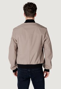 Giacca bomber da uomo in beige chiaro con colletto e polsini a costine neri. Realizzata in materiale liscio, presenta un design corto e orlo elastico.