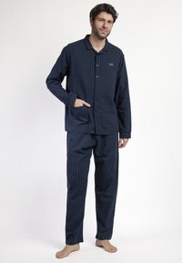 Pijamas a rayas azul marino hechos de tela suave; parte superior con botones y un bolsillo, pantalones a juego con cintura elástica, corte relajado.