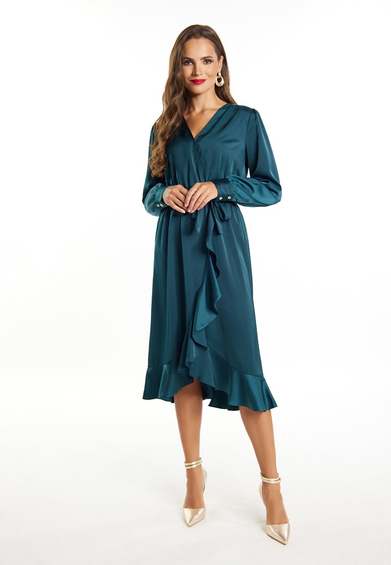 Teal satin kjole med lange ærmer, V-hals, flæset nederdel og tætsiddende talje. Accentueret med knapper på ærmerne. Sammen med guld hæle.