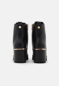 Bottines en cuir noir avec un talon épais, des fermetures éclair sur les côtés, des accents en métal doré et une semelle en caoutchouc texturée. Design élégant et moderne.