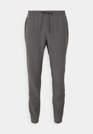 Kohlrabenschwarze Hose mit elastischem Bund und Kordelzug. Verfügt über seitliche Taschen und dunkellila Akzente an den unteren Seiten. Glatte Textur.