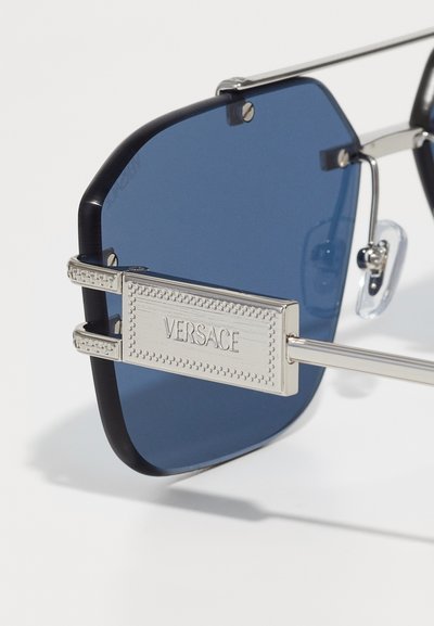 Versace prillid, millel on iseloomulikud sinised läätsed, metallaktsendid ja mustriline hõbedane raam. Omab silmapaistvat logo plaati.
