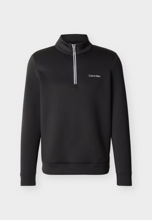 Svart langermet genser med kvartglidelås foran og høy krage, med en liten hvit "Calvin Klein"-logo på venstre bryst.