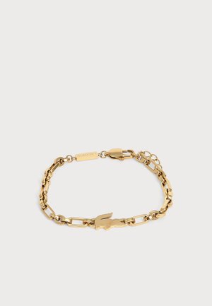 Bracelet chaîne en or avec des maillons rectangulaires et un pendentif en forme de crocodile, doté d’un fermoir mousqueton et d’une petite étiquette gravée.