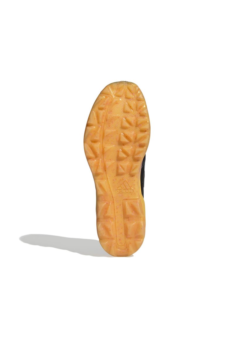 Chaussure de sport noire avec une semelle en caoutchouc jaune texturé dotée de crampons triangulaires pour l'adhérence et d'un logo Adidas en relief.