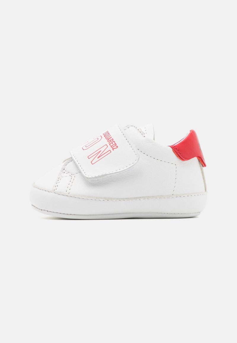 Chaussure en cuir blanc pour tout-petits avec un accent de talon rouge. Elle est dotée d'une sangle Velcro avec une lettre "N", d'un bout arrondi et de détails de couture discrets.