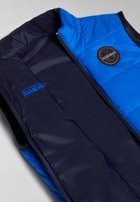 Vadderad väst med en klarblå utsida och marinblå insida. Dragkedja, rund logopatch och slät textur genomgående.