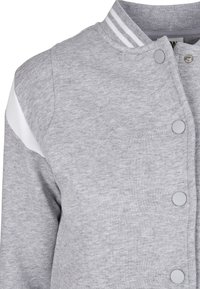 Gray cotton bomber jacket with white striped collar and panel. Features snap buttons and textured fabric for a casual look.