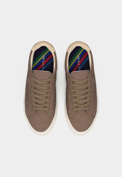 Paire de baskets beiges à lacets avec semelles blanches et semelles intérieures rayées colorées, vues de dessus sur un fond clair uni.