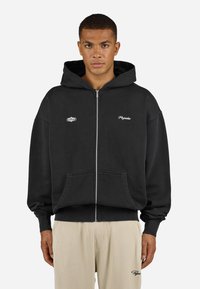 Sort zip-up hoodie lavet af blødt materiale med en stor hætte, frontlommer og hvid brodering på brystet og ærmet.