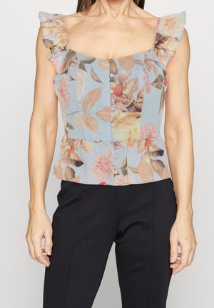 Blauwe, mouwloze blouse met bloemenmotief, gerimpelde bandjes en knopen aan de voorkant, gecombineerd met zwarte, nauwsluitende broek.