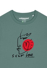 Groene katoenen t-shirt met een geprinte zwarte lijntekening van een gezicht, een rode cirkel en de tekst "SELF LOVE" in zwarte letters.