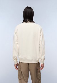 Beiges Sweatshirt mit langen Ärmeln, gerippten Bündchen und Rundhalsausschnitt. Kombiniert mit khakifarbenen Cargo-Hosen. Glatte Textur, schlichtes Design, keine sichtbaren Muster.